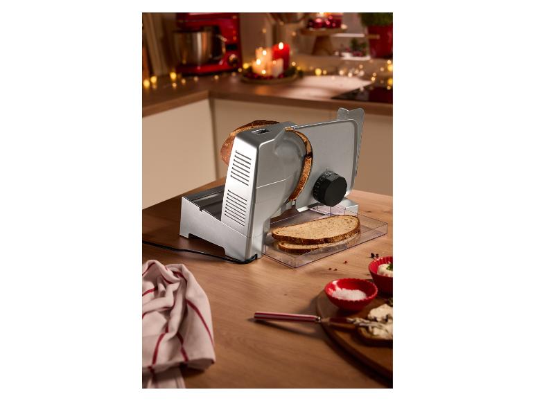 Brotschneidemaschine auf einem Holztisch, mit geschnittenem Brot und Schalen mit Salz und Käse.