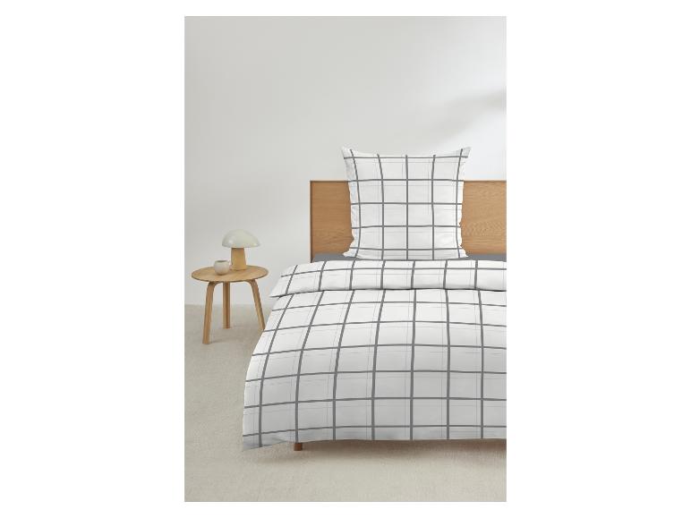 Bettwäsche mit weißem und grauem Karomuster auf einem Bett mit Holz-Kopfteil und Nachttisch.