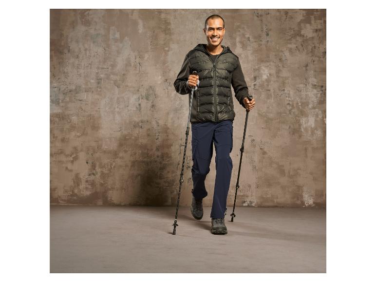 Mann in einer schwarzen Jacke und blauen Hosen mit Wanderstöcken.