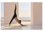 Frau macht Yoga im Freien mit Meerblick, trägt schwarze Leggings und mintgrünes Sporttop.
