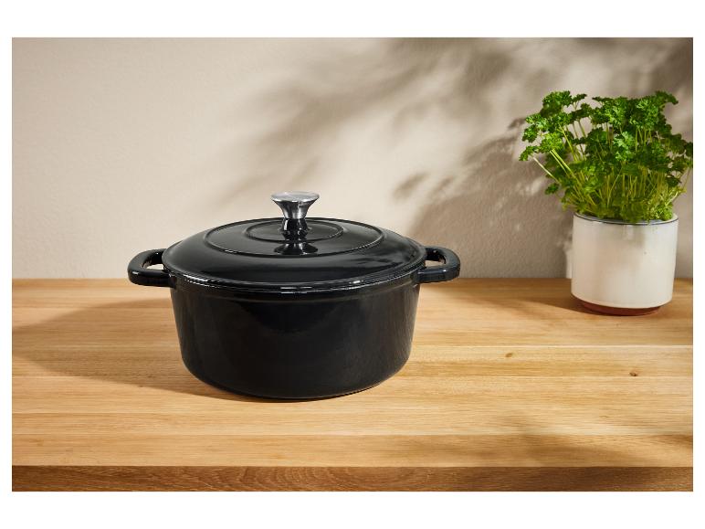 Ein schwarzer gusseiserner Topf mit Deckel auf einem Holztisch.