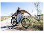 Frau mit E-Bike an einem sonnigen Tag, trägt Sonnenbrille und Freizeitkleidung.