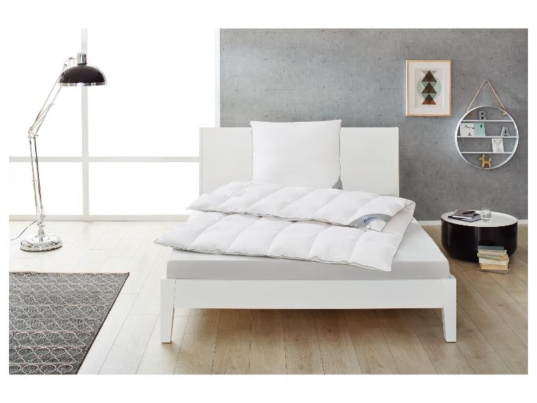 Weißes Bett mit Bettdecke und Kissen, Leselampe und Beistelltisch in einem modernen Schlafzimmer.