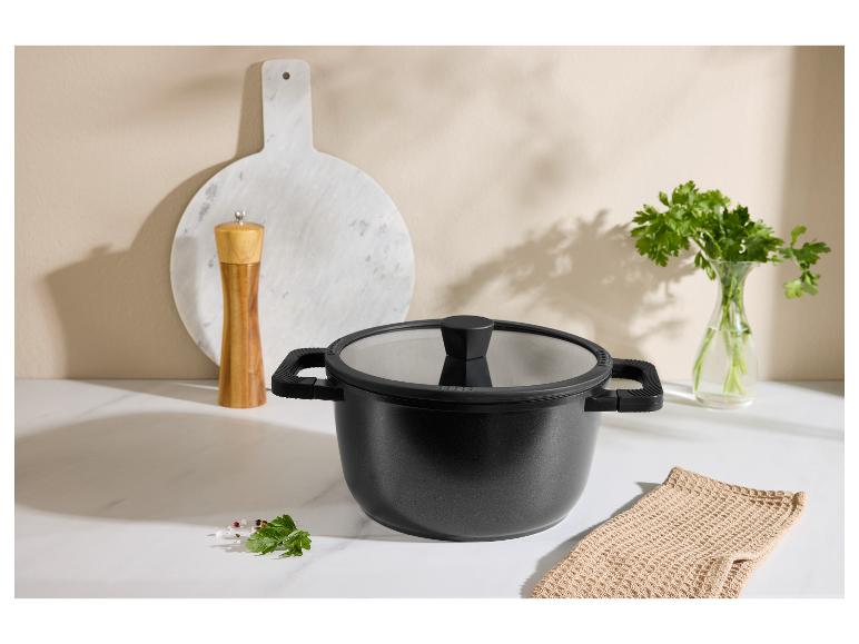 Schwarzer Topf mit Deckel, Pfeffermühle, Schneidebrett und Petersilie in der Küche.