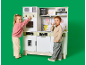 Zwei Kinder spielen mit einer großen Kinderküche aus Holz vor grünem Hintergrund.