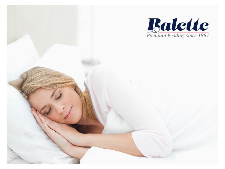 Frau schläft auf weißem Kissen und Decke, mit Balette Premium Bedding-Logo.