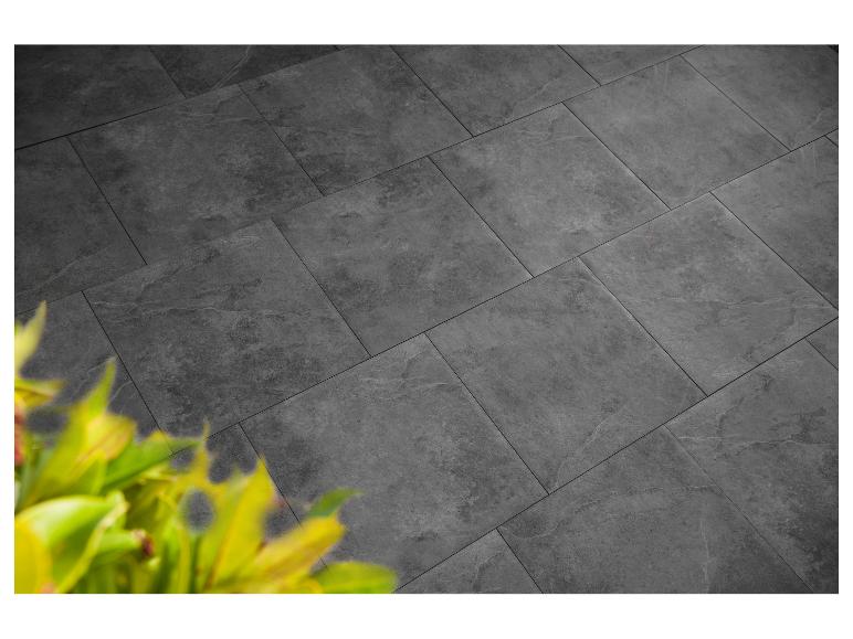 Dunkelgraue Terrassenplatten mit subtiler Textur, teilweise von grünem Laub verdeckt.