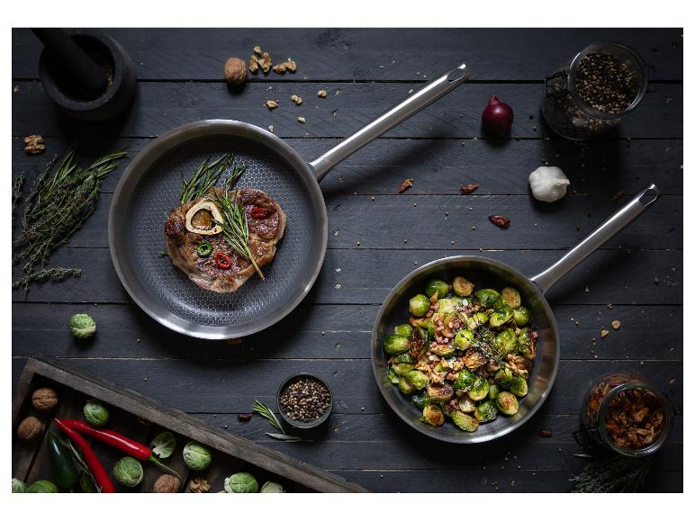Fleisch- und Rosenkohlgericht in Pfannen, mit Gewürzen und Walnüssen auf einem Holztisch.