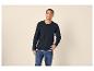 Mann in einem dunkelblauen Langarmshirt mit Knöpfen und Jeans, lächelt und schaut nach oben.
