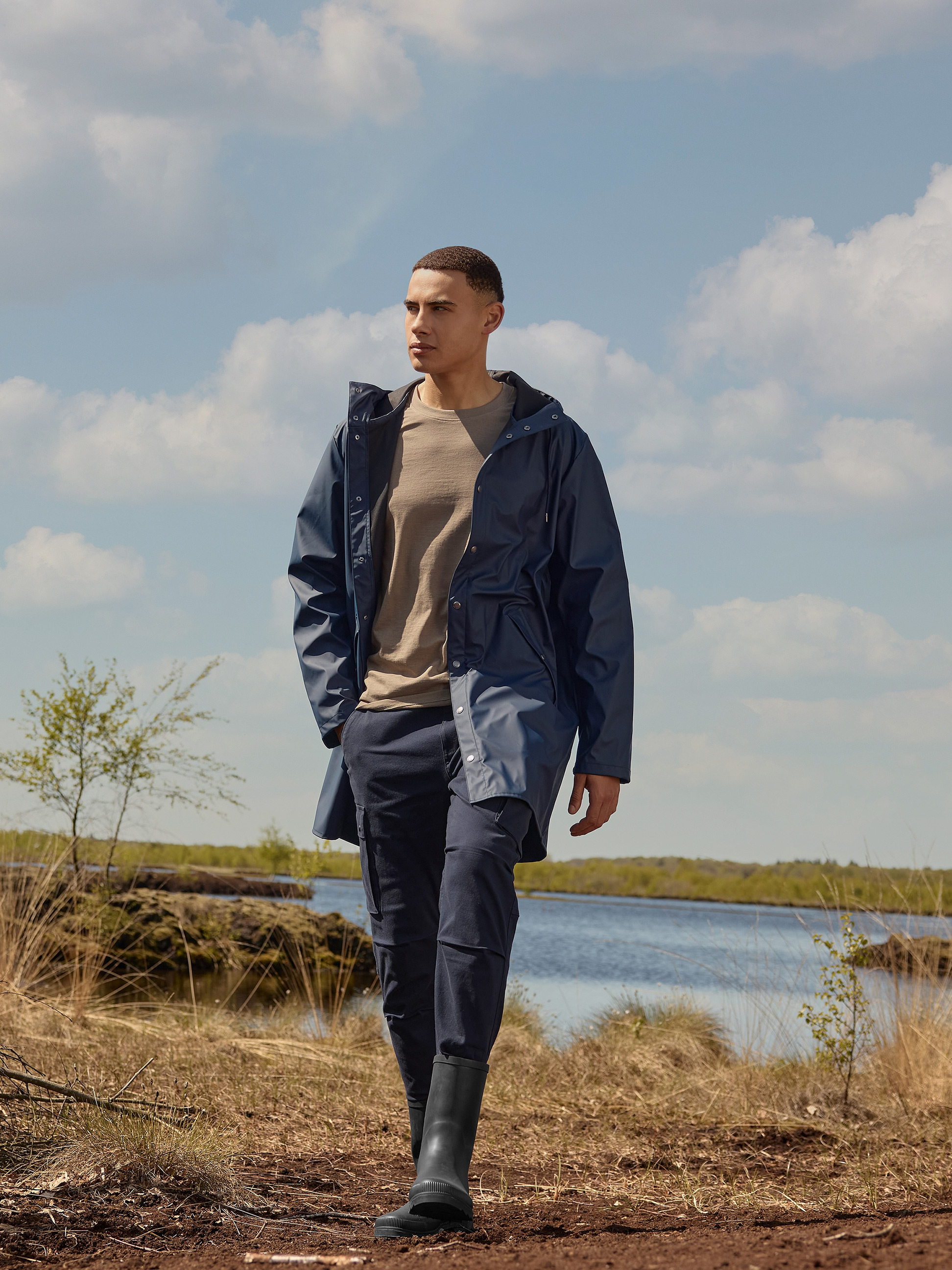 Herren-Regenmantel und -Hose in Dunkelblau, braunes T-Shirt, schwarze Gummistiefel in der Natur.