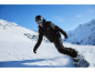Snowboarder in schwarzer Jacke und Hose, mit Helm und Brille, fährt einen verschneiten Berghang hinunter.