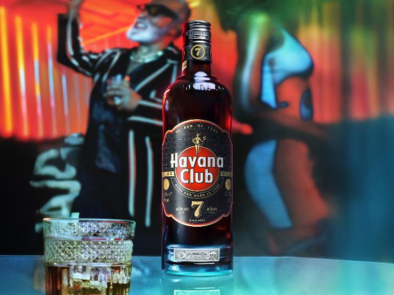 Flasche dunkler Rum und ein Glas Rum auf einem Tisch, mit verschwommenen Partygästen im Hintergrund.