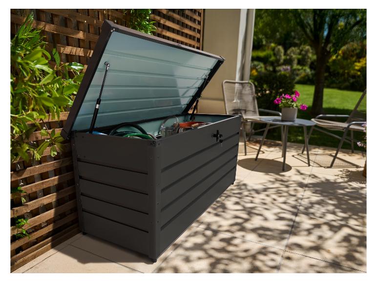 Dunkelgraue Outdoor-Aufbewahrungsbox mit offenem Deckel, gefüllt mit Gartengeräten, auf einer Terrasse.
