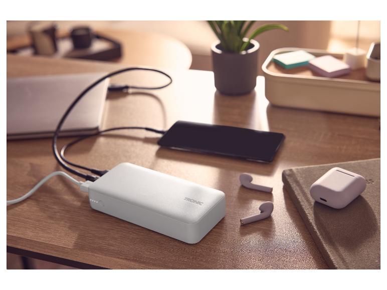 Powerbank lädt Telefon und Laptop, mit kabellosen Kopfhörern auf einem Schreibtisch.