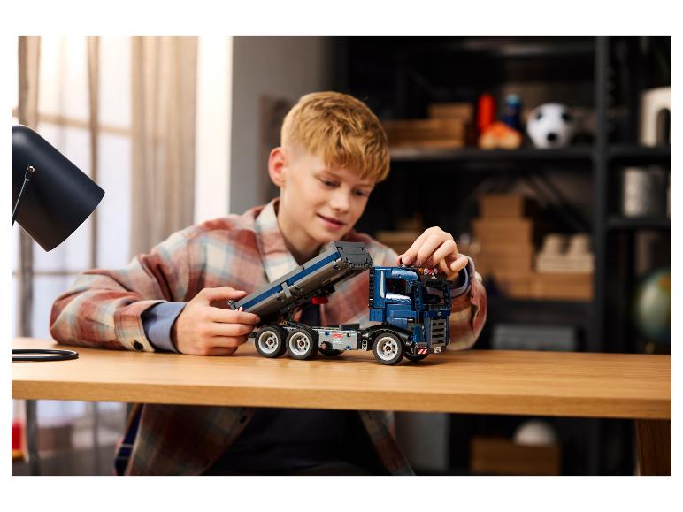 Ein Junge baut einen blauen Spielzeuglastwagen auf einem Holztisch zusammen.