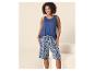 Frau in blauem Tanktop und gemusterten blau-weißen Shorts, lächelnd.