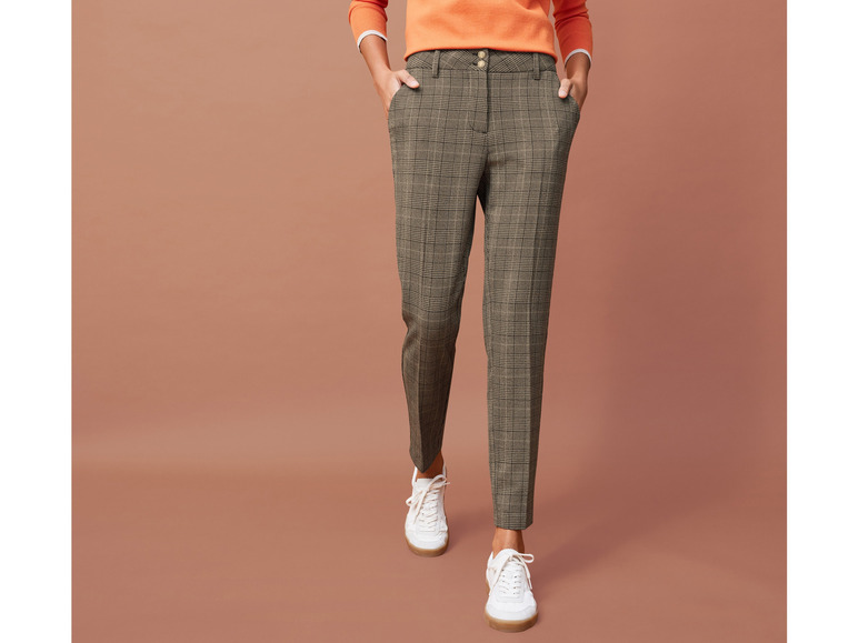 Eine Frau trägt eine karierte Hose und weiße Sneaker.