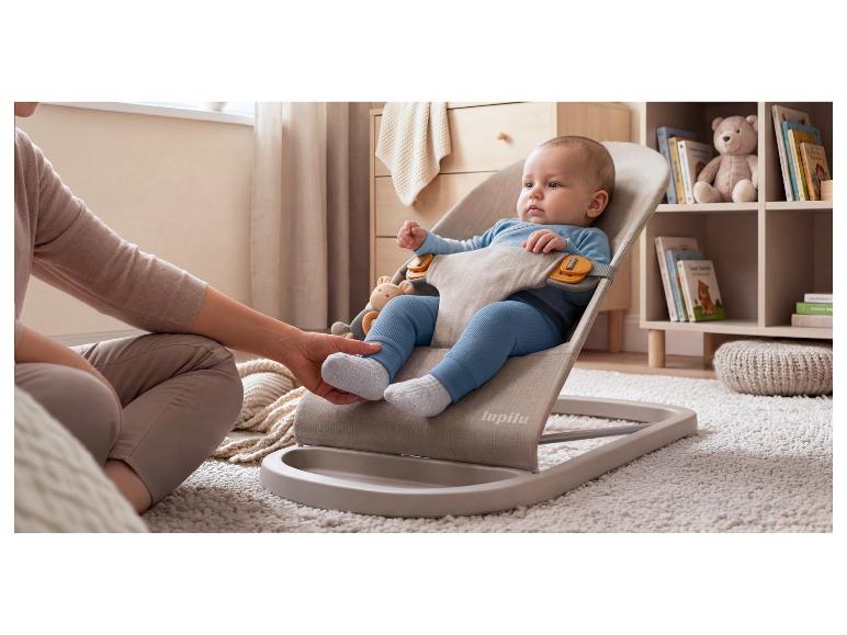 Baby in einer Wippe, mit der Hand eines Erwachsenen, die den Fuß des Babys berührt, auf einem flauschigen Teppich.