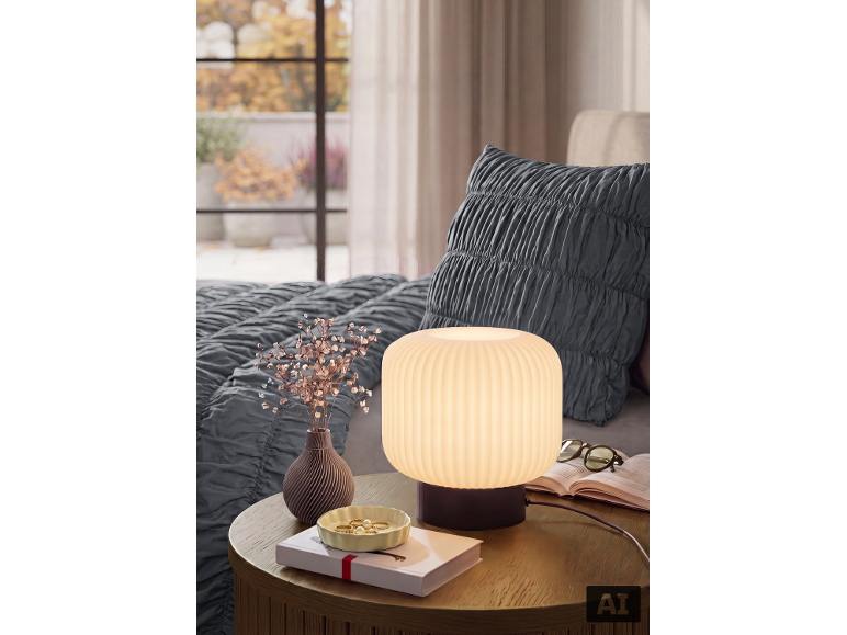 Nachttisch mit Lampe, Vase mit Trockenblumen, Schmuckschale und Buch neben einem Bett.