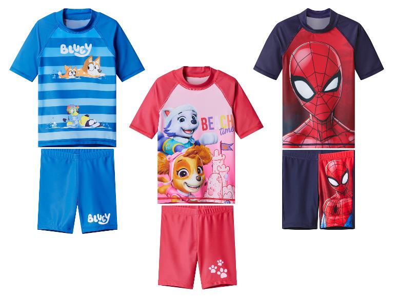 Drei Sets Kinder-Badebekleidung: blau mit Cartoon-Hunden, pink mit Cartoon-Welpen und rot/marineblau mit einem Superhelden.