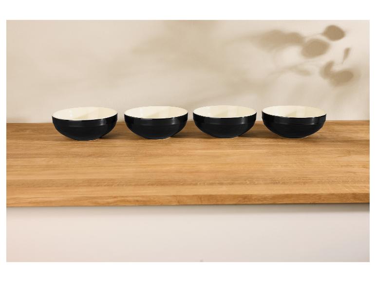 Vier schwarze Schalen auf einem hellen Holztisch, mit Blattschatten an der Wand.
