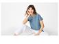 Frau in blauem besticktem T-Shirt und weißer Hose, sitzend.