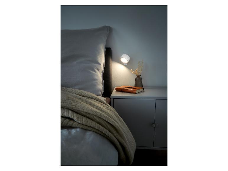Ein Bett mit Bettdecke, ein Nachttisch mit einem Buch und einer Philips Hue Lampe.