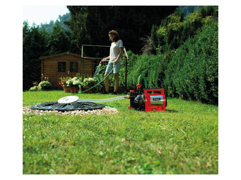 Frau bewässert Garten mit einer Gartenpumpe, die an einen Wassertank angeschlossen ist.