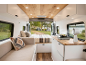 Van-Interieur mit Küche, Bett und Sofa, Blick auf einen Campingplatz am See.