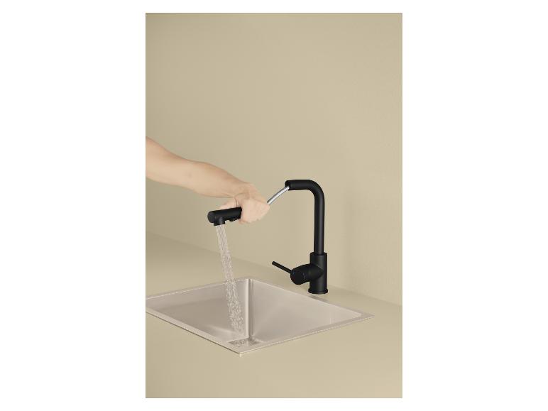 Hand hält eine schwarze Küchenarmatur mit ausziehbarer Brause über einem Edelstahlspülbecken.