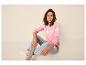 Frau sitzt in rosa Pullover und Jeans, lächelnd in die Kamera.