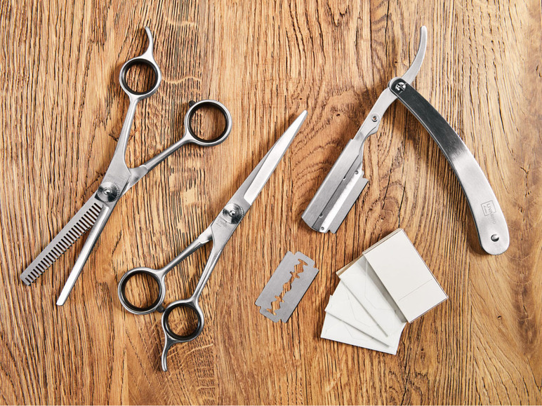 Zwei Scheren, ein Rasiermesser und Rasierklingen auf einer Holzoberfläche.