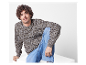 Mann in meliertem Pullover und Jeans sitzt auf einer weißen Oberfläche.
