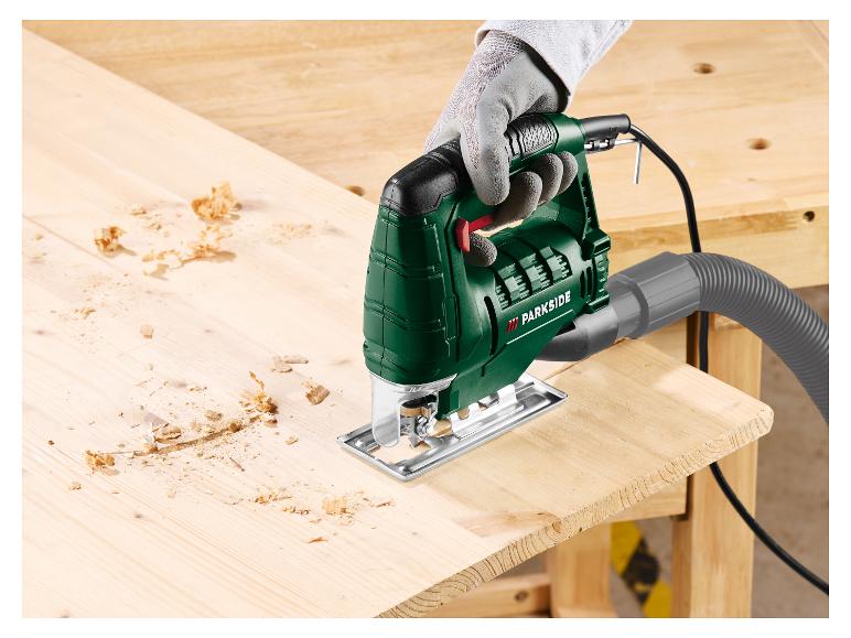 Grüne Parkside Stichsäge schneidet ein Holzbrett, mit Spänen.