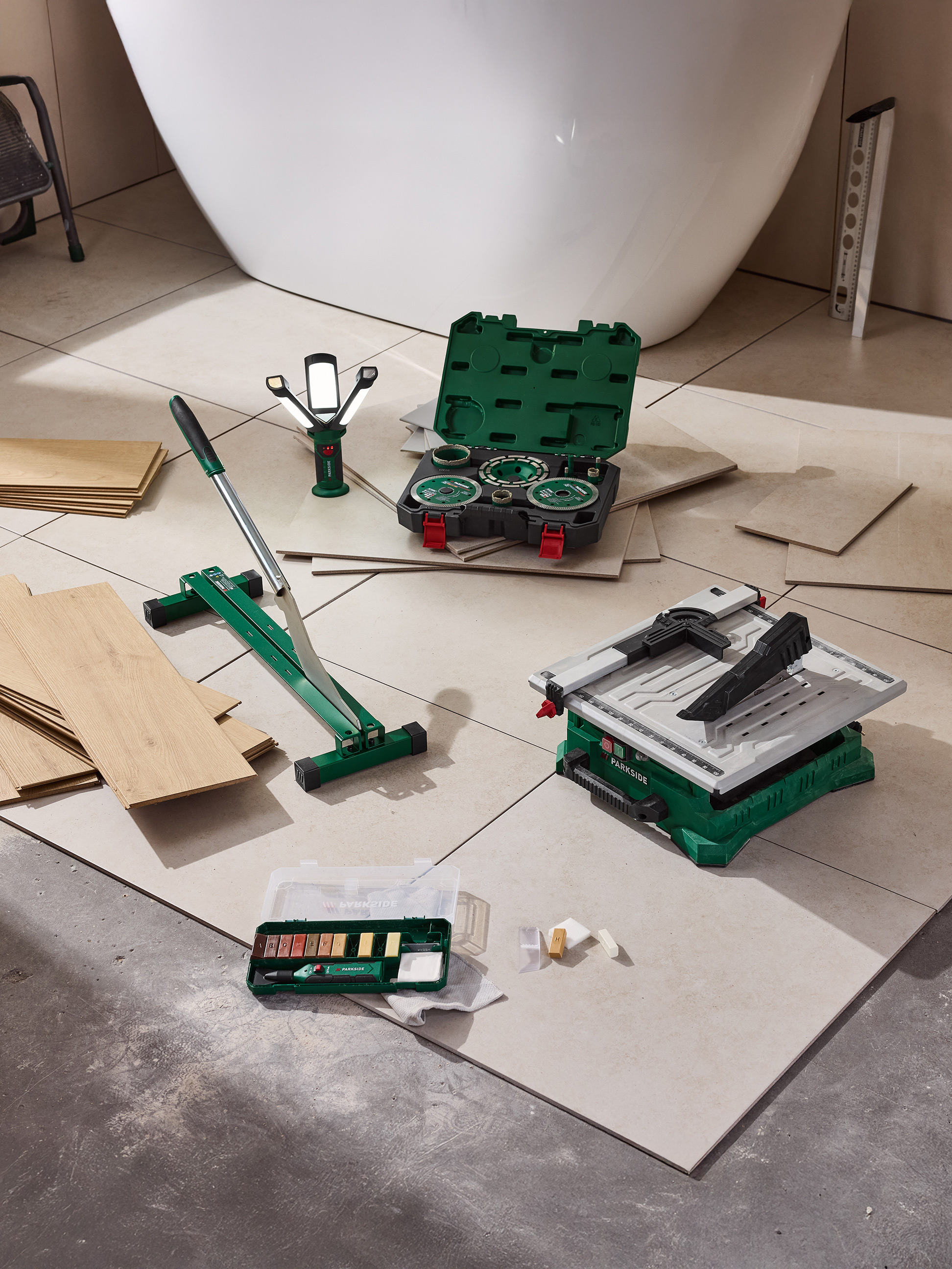 Parkside Fliesenschneider, Fliesensäge und Reparaturset auf Fliesenboden neben einer Badewanne.