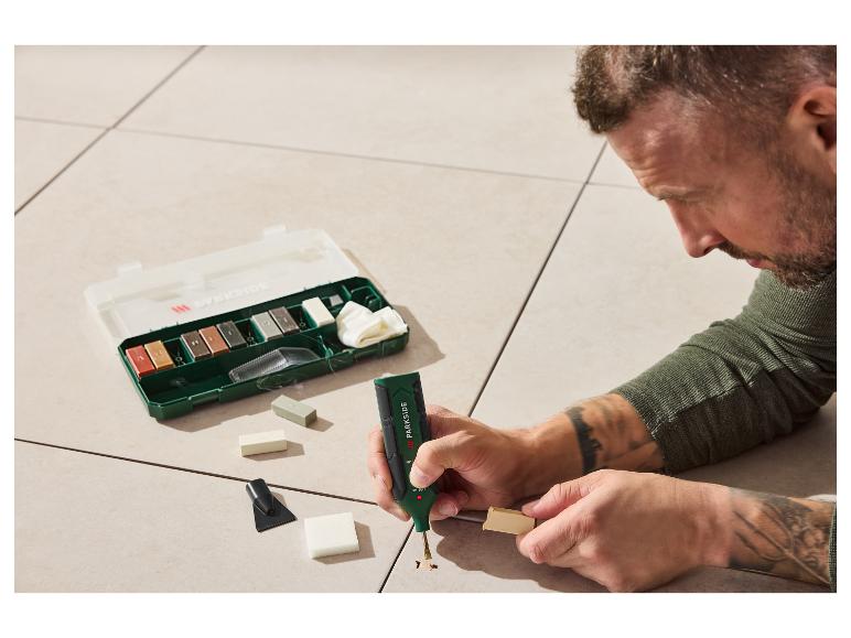 Mann benutzt ein PARKIDE Reparaturset, um ein Loch in einem hellen Boden zu füllen.