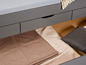 Ein graues Bett mit drei Schubladen und Decken in der Schublade.