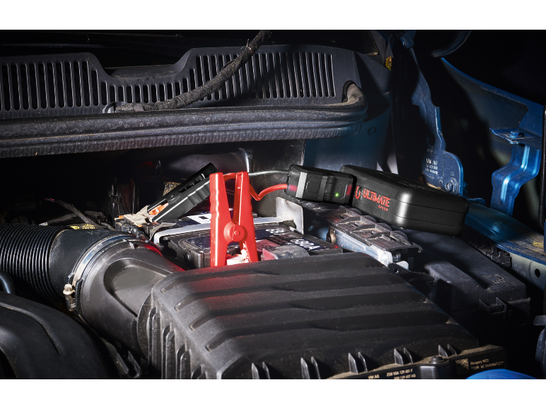 Motorraum mit Starthilfekabeln, die an eine Autobatterie angeschlossen sind.