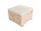 Geflochtener Outdoor-Hocker mit cremefarbenem Kissen.