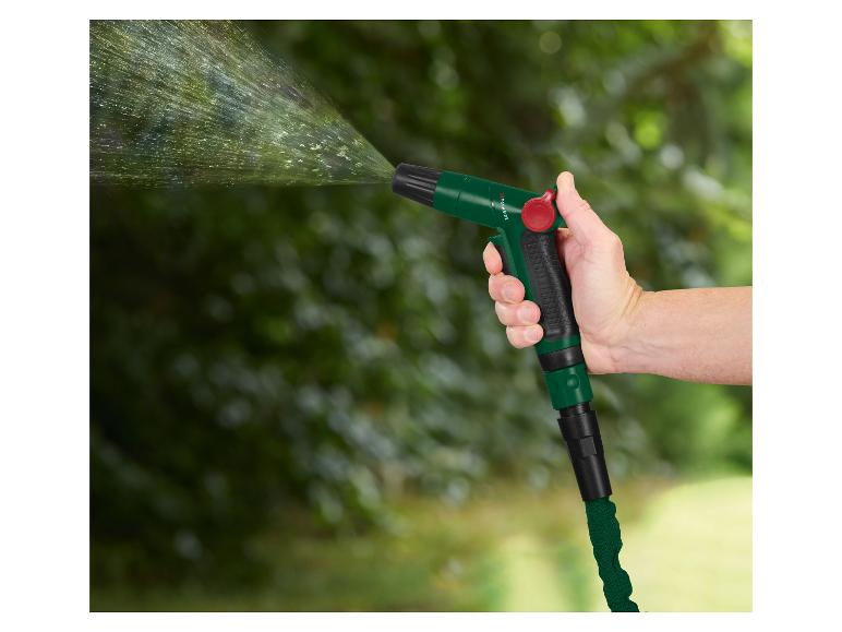 Hand hält eine grüne Gartenschlauchdüse, die Wasser sprüht, mit verschwommenem grünem Hintergrund.