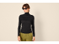 Frau in schwarzem Rollkragenpullover und grüner Hose, Sonnenbrille.