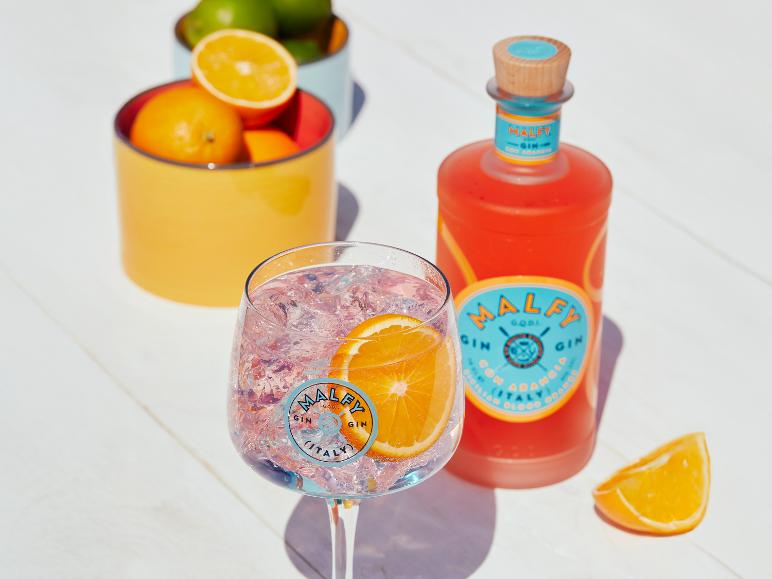 Pinker Gin-Cocktail mit Orangenscheibe, Gin-Flasche und Schalen mit Zitrusfrüchten.