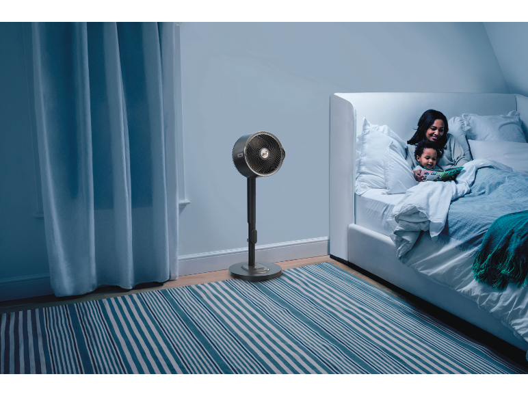 Standventilator in einem Schlafzimmer mit Mutter und Kind, die im Bett lesen.