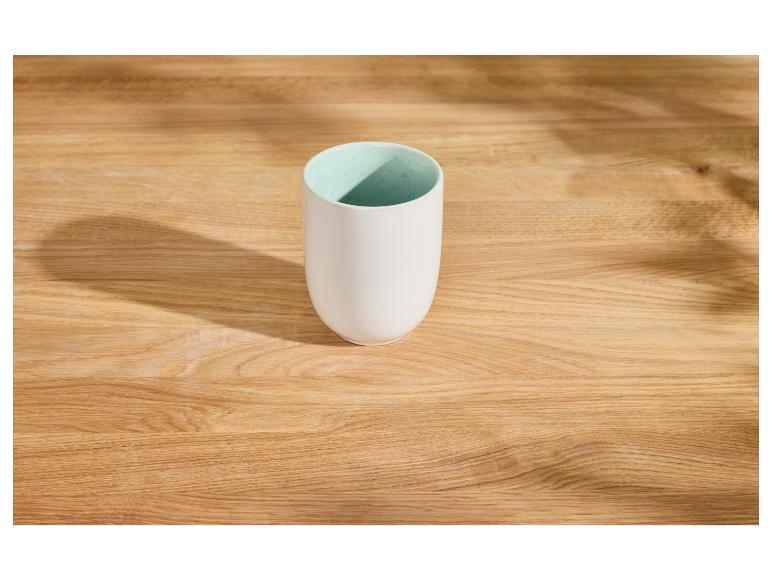 Weiße Keramiktasse mit hellblauer Innenseite auf einem Holztisch mit Schatten.