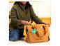 Lächelnde Frau in grünem Pullover legt ein Winnie Puuh-Spielzeug in eine braune Wickeltasche.
