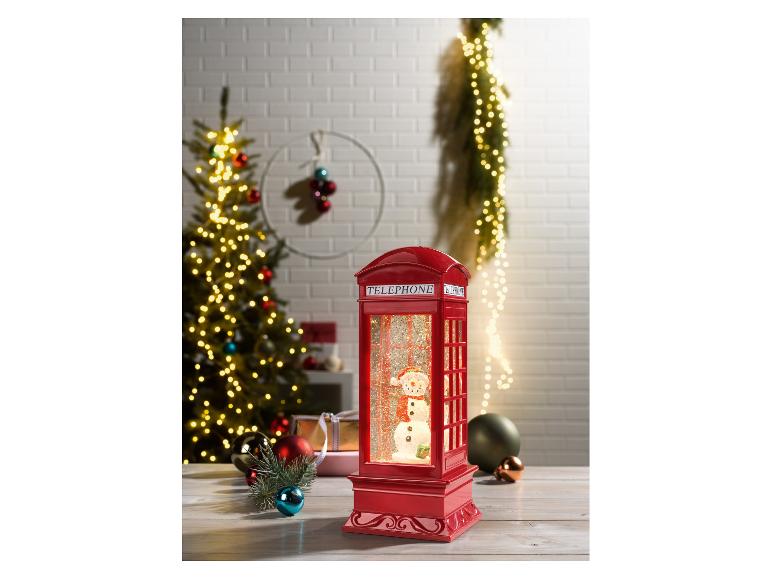 Eine rote Telefonzellen-Schneekugel mit einem Schneemann darin, umgeben von Weihnachtsdekorationen.