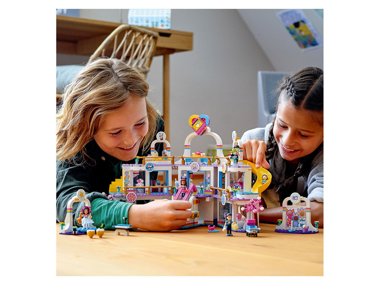 Zwei Kinder spielen mit einem LEGO Friends Einkaufszentrum mit Rutsche und Karussell.