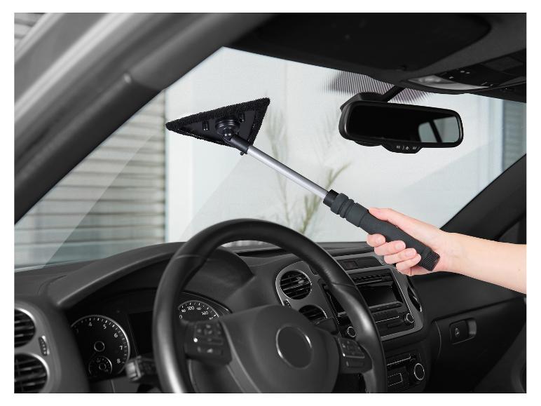 Person reinigt die Windschutzscheibe eines Autos von innen mit einem Reiniger mit Stiel.