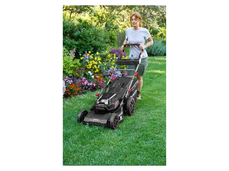 Frau mäht Rasen mit einem Parkside Rasenmäher in einem blühenden Garten.