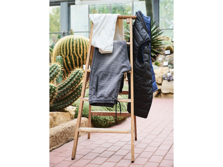 Eine graue Hose, ein weißes Oberteil und eine schwarze Weste hängen an einer Holzleiter.